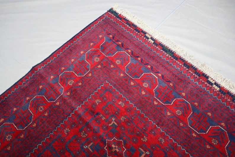 May include: A red and blue patterned rug with a white fringe. The rug has a geometric design with intricate details.