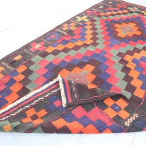 May include: A colorful geometric rug with a traditional design. The rug is made of wool and has a fringe border. The rug is folded in half, showing the intricate pattern.