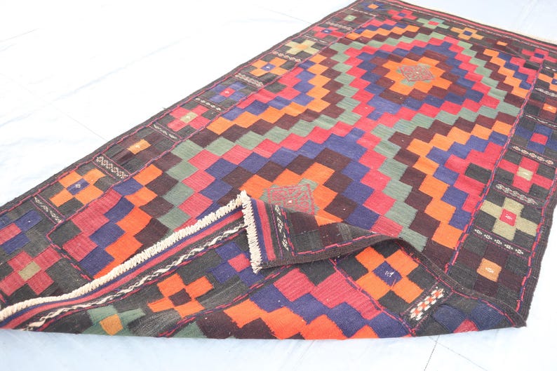 May include: A colorful geometric rug with a traditional design. The rug is made of wool and has a fringe border. The rug is folded in half, showing the intricate pattern.