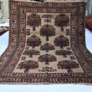 May include: A large, rectangular rug with an intricate floral design. The rug features a beige background with repeating tree-like motifs in red, blue, and brown. The border is a darker brown with geometric patterns. The rug is displayed on a white surface.