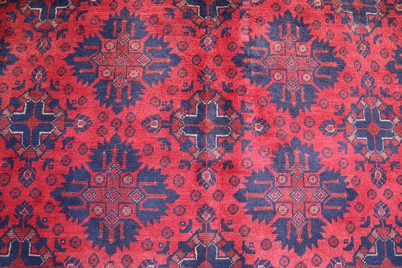 May include: A red rug with a repeating pattern of blue and white geometric shapes. The rug has a traditional design.