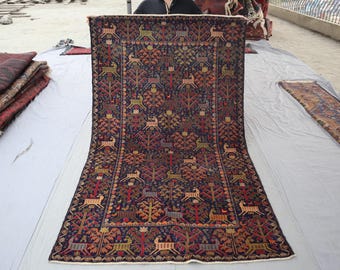 May include: A rectangular, hand-woven rug with a dark blue background and a repeating pattern of deer and trees in shades of red, orange, and green. The rug has a detailed border and a traditional design.