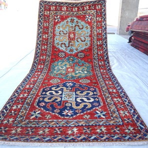May include: A red, blue, and green patterned rug with intricate designs. The rug has a fringe border and is folded in half.