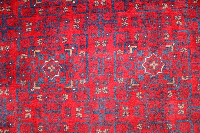 May include: A red rug with a blue and white geometric pattern. The rug has a traditional design with repeating motifs.