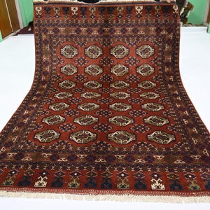 May include: A large, rectangular rug with an intricate geometric pattern. The rug features a deep red background with repeating medallions in shades of brown, green, and cream. The border and fringe are visible.