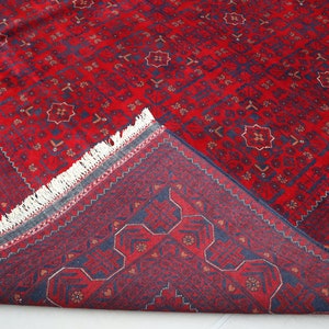 May include: A red and blue patterned rug with a fringe border. The rug is folded in half, showing the back side.