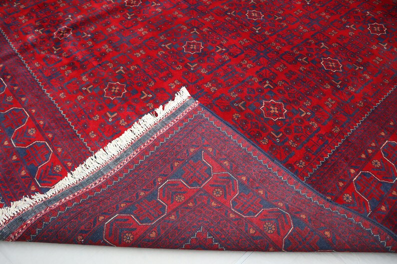 May include: A red and blue patterned rug with a fringe border. The rug is folded in half, showing the back side.