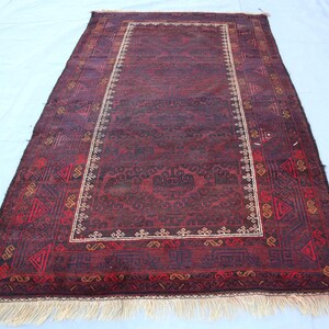May include: A dark red rug with a geometric pattern and a cream-colored border. The rug has a fringe on all sides.