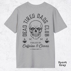 May include: A sport grey t-shirt featuring a black graphic print of a skull with Zs in the eye sockets. The text reads DEAD TIRED DADS CLUB, FUELED BY Caffeine & Chaos, and SINCE 2024, accompanied by two coffee cup icons and small crossbones.