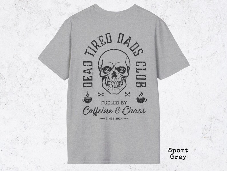 May include: A sport grey t-shirt featuring a black graphic print of a skull with Zs in the eye sockets. The text reads DEAD TIRED DADS CLUB, FUELED BY Caffeine & Chaos, and SINCE 2024, accompanied by two coffee cup icons and small crossbones.