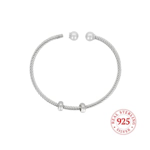 May include: A silver-colored bangle bracelet with a twisted cable design. The bracelet has two small, round beads and two cylindrical beads. The end of the bracelet has a screw closure. A circular stamp reads "REAL STERLING 925 SILVER."