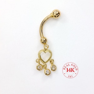 May include: A gold-colored belly button ring with a curved barbell design. The ring features a heart-shaped charm with a white center and three dangling clear gemstones. The image includes a red stamp that reads "REAL GOLD 14K 585".