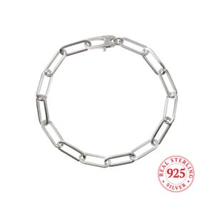 May include: A silver chain bracelet with a lobster clasp closure. The chain is made of oval links. The bracelet is stamped "REAL STERLING 925 SILVER".