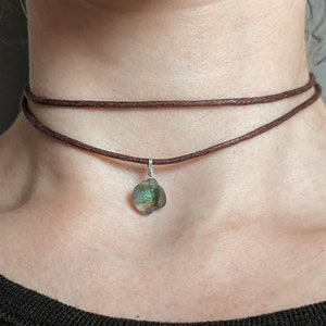 May include: A brown leather choker necklace with a silver chain and a green gemstone pendant.