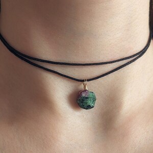 Könnte beinhalten: Eine schwarze Choker-Kette mit einem grünen und rosafarbenen Edelstein-Anhänger.