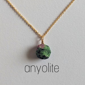 May include: A gold chain necklace with a green and pink anyolite pendant. The pendant is a rough, natural stone.