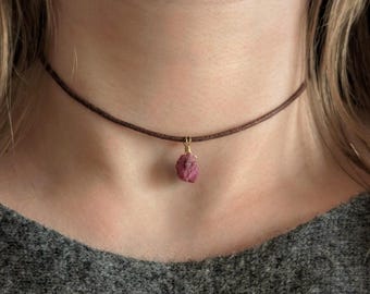 Może przedstawiać: Brązowy skórzany naszyjnik choker z małym, różowym, surowym wisiorem z rubinu.