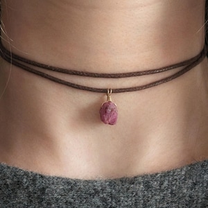 Könnte beinhalten: Eine braune Lederkette mit einem rosa Edelstein-Anhänger.