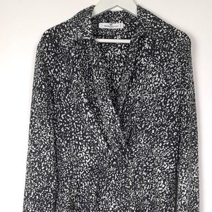 Puede incluir: Blusa de manga larga con estampado moteado en blanco y negro. La blusa tiene cuello y un frente cruzado. La tela est&aacute; cubierta con un dise&ntilde;o moteado. La blusa est&aacute; colgada en una percha blanca.