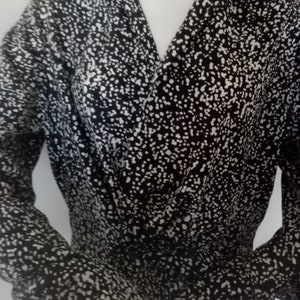 Puede incluir: Top envolvente con estampado en blanco y negro con mangas largas. La tela est&aacute; cubierta de peque&ntilde;os puntos blancos sobre un fondo negro. El top tiene un escote en V y se muestra en un maniqu&iacute;.