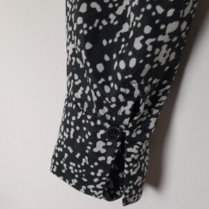 Puede incluir: Primer plano de una manga con estampado en blanco y negro. La tela presenta un patr&oacute;n repetitivo de puntos blancos sobre un fondo negro. El pu&ntilde;o est&aacute; abotonado y la manga est&aacute; ligeramente doblada.