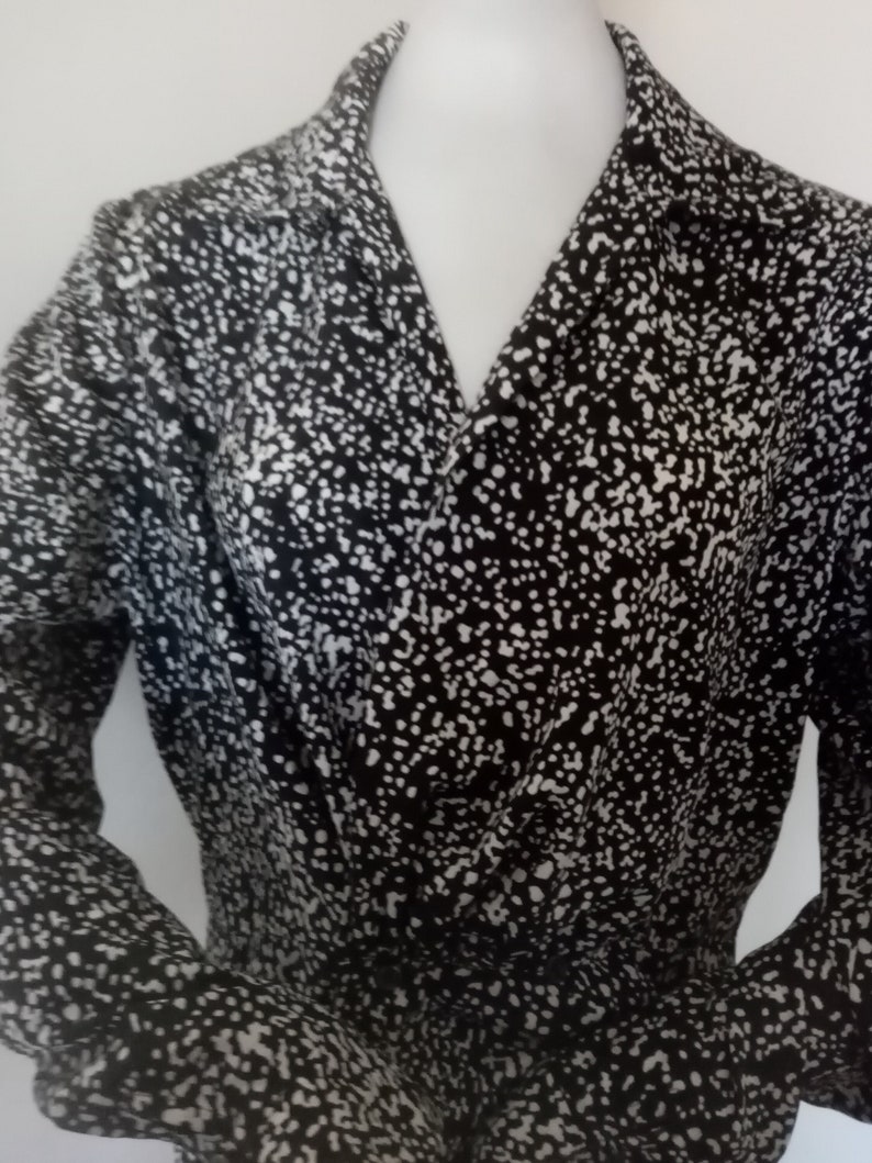 Puede incluir: Top envolvente con estampado en blanco y negro con mangas largas. La tela est&aacute; cubierta de peque&ntilde;os puntos blancos sobre un fondo negro. El top tiene un escote en V y se muestra en un maniqu&iacute;.