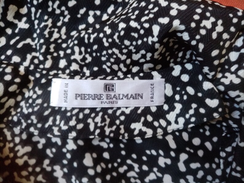 Puede incluir: Tejido estampado en blanco y negro con un dise&ntilde;o de lunares repetido. La etiqueta dice "PIERRE BALMAIN PARIS FRANCE" y "MADE IN FRANCE". El tejido tiene un aspecto sedoso.