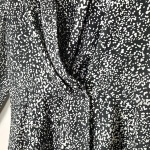 Puede incluir: Top con estampado en blanco y negro con cuello drapeado y cierre de botones. La tela presenta un dise&ntilde;o moteado, creando una apariencia texturizada. El top tiene mangas largas y un ajuste entallado, adecuado para diversas ocasiones.