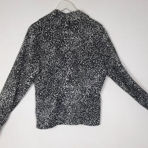 Puede incluir: Una camisa de manga larga con estampado en blanco y negro. La camisa est&aacute; colgada de una percha blanca sobre un fondo blanco. El estampado es un dise&ntilde;o moteado, con peque&ntilde;os puntos blancos sobre una base negra.