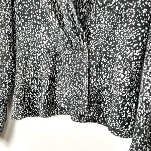 Puede incluir: Blusa estampada en blanco y negro con parte delantera cruzada y cierre de botones. La tela presenta un dise&ntilde;o moteado, creando una apariencia texturizada. La parte superior de manga larga tiene un dobladillo ligeramente acampanado.