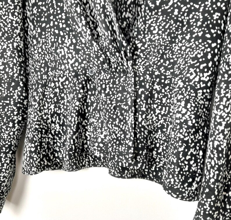 Puede incluir: Blusa estampada en blanco y negro con parte delantera cruzada y cierre de botones. La tela presenta un dise&ntilde;o moteado, creando una apariencia texturizada. La parte superior de manga larga tiene un dobladillo ligeramente acampanado.
