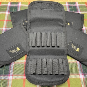 Könnte beinhalten: Schwarze Stoff-Rolltasche mit mehreren Fächern zur Aufbewahrung. Die Tasche ist offen und zeigt mehrere Reihen elastischer Schlaufen. Drei zusätzliche geschlossene Taschen sind ebenfalls sichtbar. Jede Tasche hat ein kleines rechteckiges Etikett mit Text und Vogellogo.