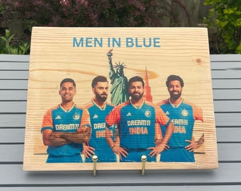May include: A wooden sign with the text "MEN IN BLUE" printed on it. The sign features a photo of four men wearing blue and orange jerseys with the text "DREAM11 INDIA" printed on them. The men are standing in front of a statue of the Statue of Liberty.