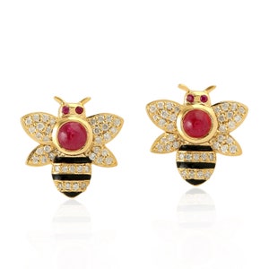 May include: A pair of gold bee earrings with black and white stripes, red ruby accents, and clear cubic zirconia stones.