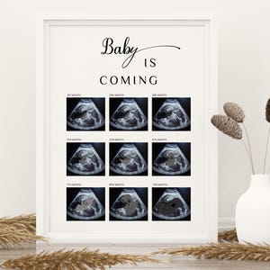 Puede incluir: Un póster enmarcado blanco con el texto "Baby is Coming" y una cuadrícula de nueve imágenes de ultrasonido que muestran el desarrollo de un bebé en el útero desde el primer hasta el noveno mes.