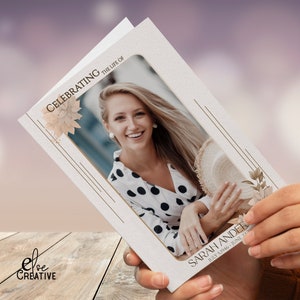 Op de afbeelding: Een witte rouwkaart met een gouden rand en bloemmotieven. In het midden van de kaart staat een foto van een lachende vrouw. De tekst "Celebrating the life of Sarah Ander July 3, 1946 - June 22, 2023" staat onderaan de kaart.