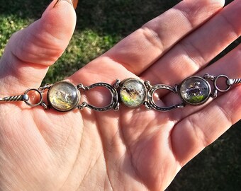 May include: A silver bracelet with four round glass charms, each featuring a different image. The charms are connected by silver horseshoe-shaped links.