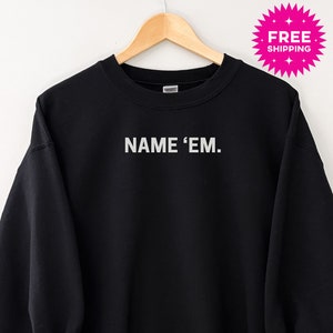 Puede incluir: Sudadera negra con el texto "NAME 'EM." impreso en blanco en la parte delantera.