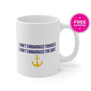 May include: White ceramic mug with a handle. The mug features the text "1. DON'T EMBARRASS YOURSELF 2. DON'T EMBARRASS THE BOAT" in navy blue, along with a gold anchor graphic. A pink starburst graphic with the words "FREE SHIPPING" is visible.