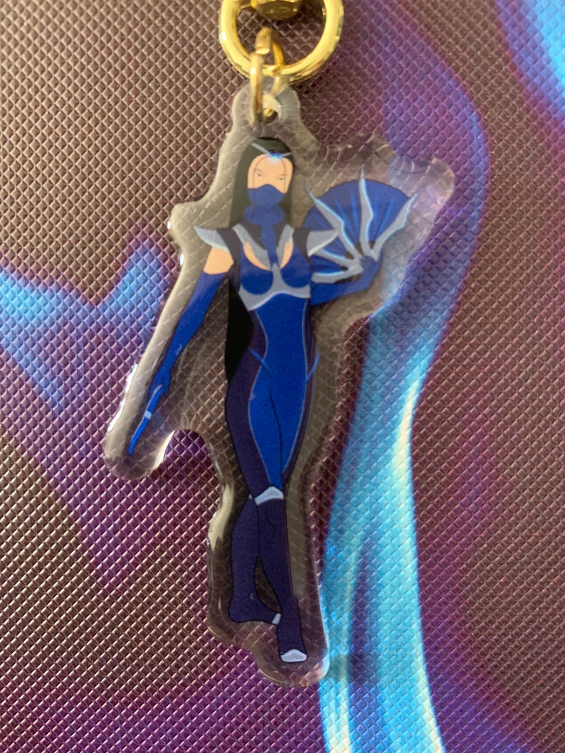 May include: A blue and white character with a fan, printed on a clear acrylic keychain with a gold metal ring.