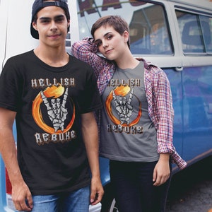 K&ouml;nnte beinhalten: Zwei Personen tragen T-Shirts mit einem Grafikdruck einer Skeletthand, die ein Rock'n'Roll-Zeichen in einem Feuerkreis macht. Der Text auf den Shirts lautet "Hellish Rebuke".