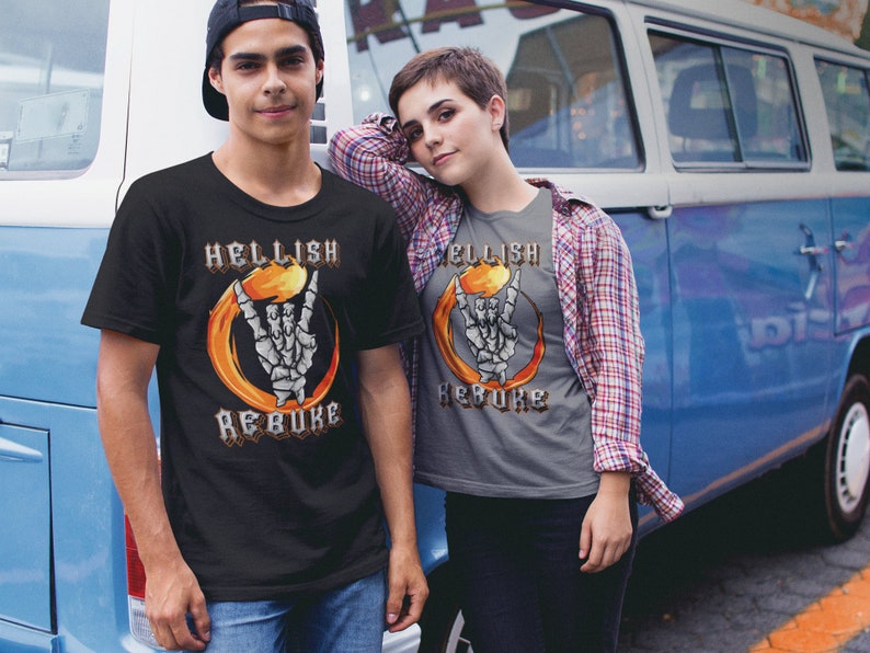 K&ouml;nnte beinhalten: Zwei Personen tragen T-Shirts mit einem Grafikdruck einer Skeletthand, die ein Rock'n'Roll-Zeichen in einem Feuerkreis macht. Der Text auf den Shirts lautet "Hellish Rebuke".