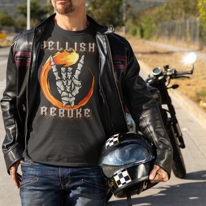 K&ouml;nnte beinhalten: Ein Mann tr&auml;gt ein schwarzes T-Shirt mit einem Grafikdruck einer Skeletthand, die das Rock'n'Roll-Zeichen mit Flammen dahinter macht. Der Text "Hellish Rebuke" ist auf das Shirt gedruckt. Er tr&auml;gt eine schwarze Lederjacke und eine blaue Jeans. Er h&auml;lt einen schwarzen Motorradhelm mit einem karierten Streifen.