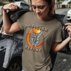 K&ouml;nnte beinhalten: Ein braunes T-Shirt mit einem Grafikdruck einer Skeletthand, die das Rock'n'Roll-Zeichen in einem Feuerkreis macht. Der Text "HELLISH REBUKE" ist in gotischer Schrift um den Kreis herum geschrieben.