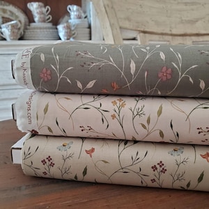 May include: Three rolls of floral fabric in shades of green, cream, and beige. Each roll features a delicate pattern of flowers and vines. The fabric is labeled with the text "Designs.com".