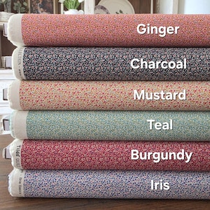 Puede incluir: Una pila de rollos de tela en varios colores, incluyendo jengibre, carbón, mostaza, verde azulado, borgoña e iris. Cada rollo muestra un patrón floral y está etiquetado con su nombre de color. La tela está bien enrollada.