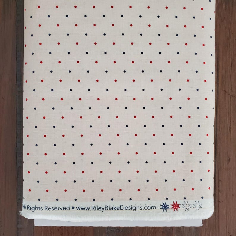 May include: A roll of fabric featuring a cream-coloured background adorned with a repeating pattern of red and navy blue polka dots. The fabric has the text "All Rights Reserved &bull; www.RileyBlakeDesigns.com".
