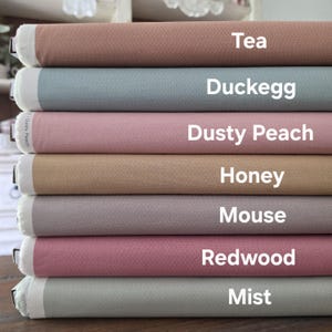 Puede incluir: Una pila de rollos de tela en varios colores, incluyendo té, duckegg, melocotón empolvado, miel, ratón, secuoya y niebla. Cada rollo está etiquetado con su nombre de color en texto blanco. La tela tiene una apariencia texturizada.