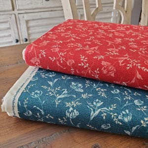 May include: Two fabric rolls, one red and one teal, with a floral pattern. The red fabric has a textured appearance, while the teal fabric has a denim-like texture. Both fabrics feature a white floral design.