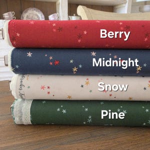 Puede incluir: Cuatro rollos de tela en tonos rojo, azul marino, crema y verde, cada uno adornado con un patrón de constelación. Los rollos están etiquetados como "Berry", "Midnight", "Snow" y "Pine". La tela tiene una apariencia texturizada y un ribete de encaje.